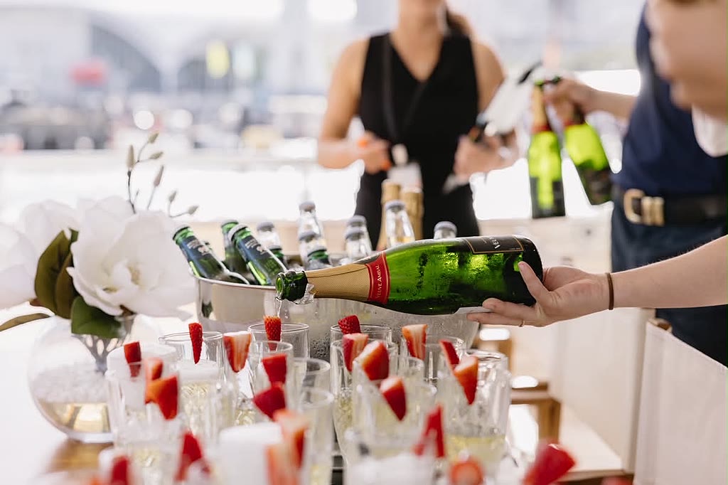 Champagne poured into glasses garnished with strawberries at a welcome station.
