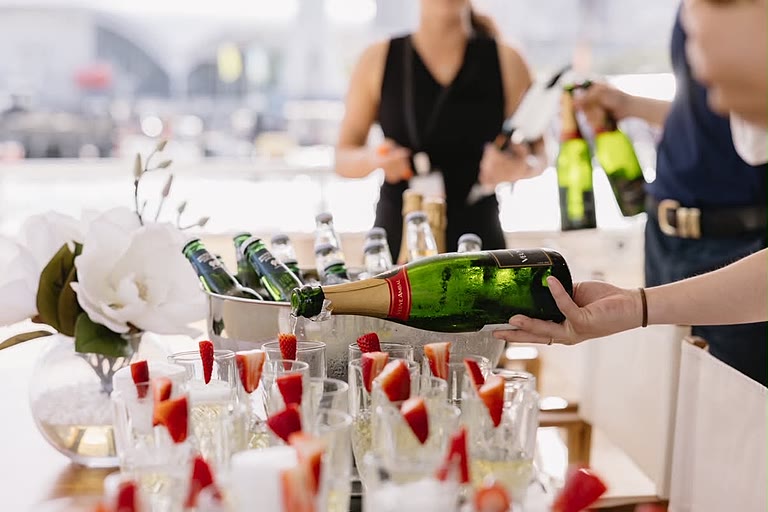 Champagne being poured into glasses garnished with strawberries at a welcome station.