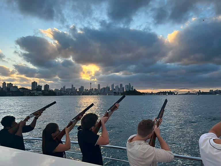 Guests taking part in a supervised clay target shooting activity at sunset, with the Sydney skyline behind.
