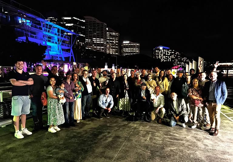 A large group of guests photographed together on the waterfront at Darling Harbour after an event.