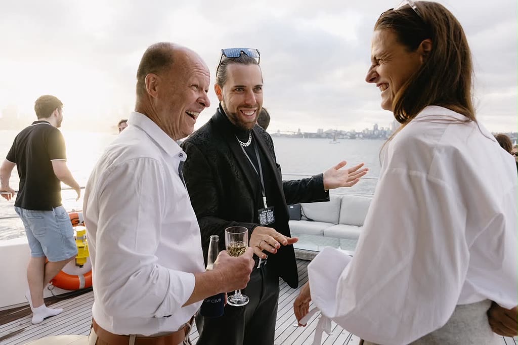 Three guests laughing together on the deck of a charter boat on Sydney Harbour at golden hour.